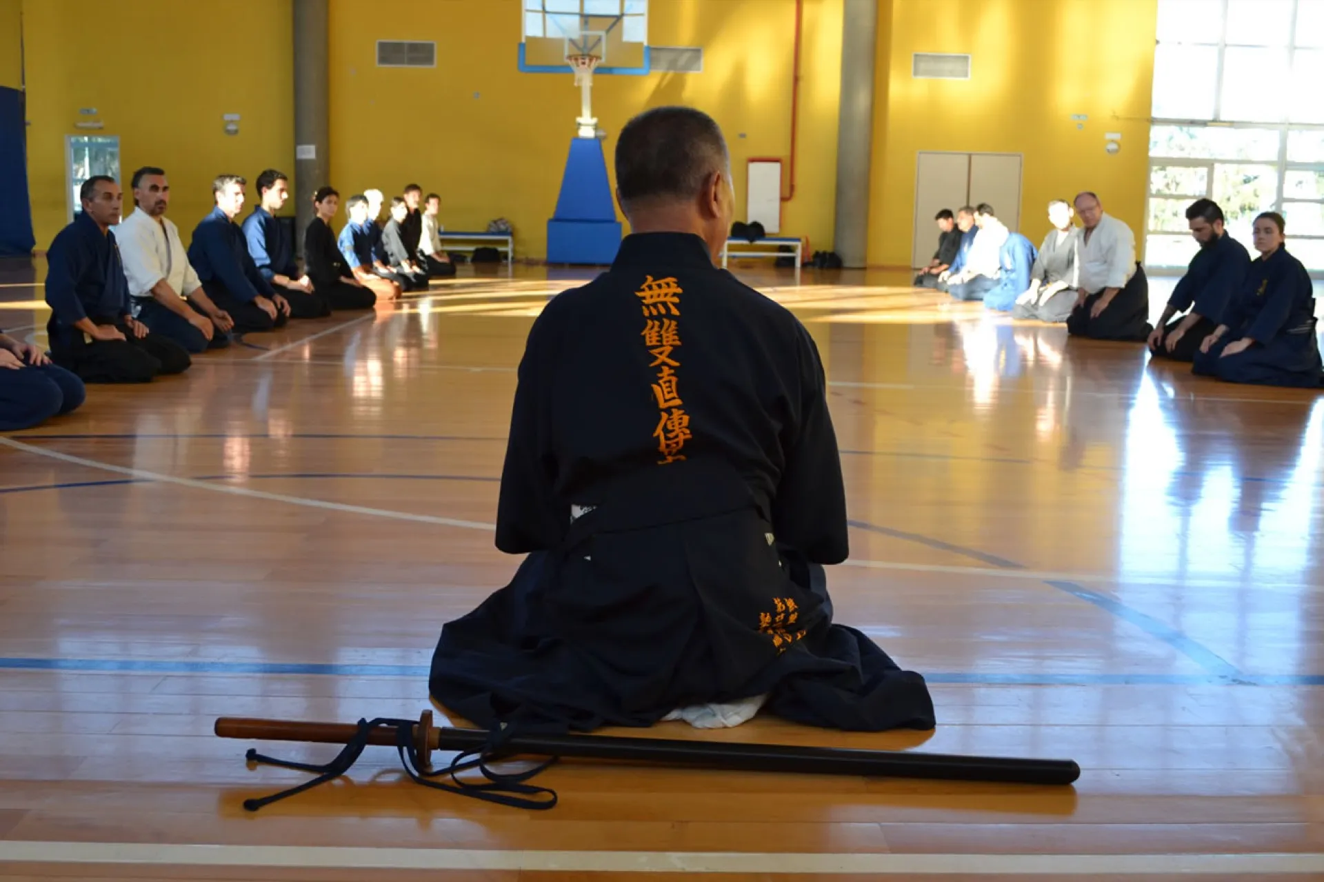 Sekiguchi Takaaki Komei sensei sentado en seiza frente a la clase, con el nombre de la escuela bordado en su gi